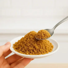 Įkelti vaizdą į galerijos rodinį, Close-up of brown sugar granules on a white plate with a spoon scooping some granules