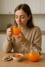 Įkelti vaizdą į galerijos rodinį, Woman enjoying hot sea buckthorn tea with fresh sea buckthorn berries and ginger on wooden table